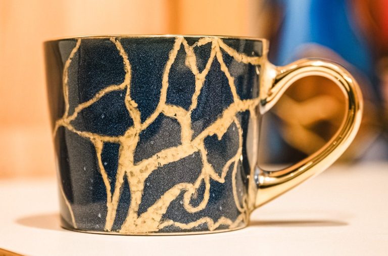 Une tasse noire réparée selon l'art japonais du Kintsugi.Les fissures dorées symbolisent la force,la résilience et la beauté née des épreuve